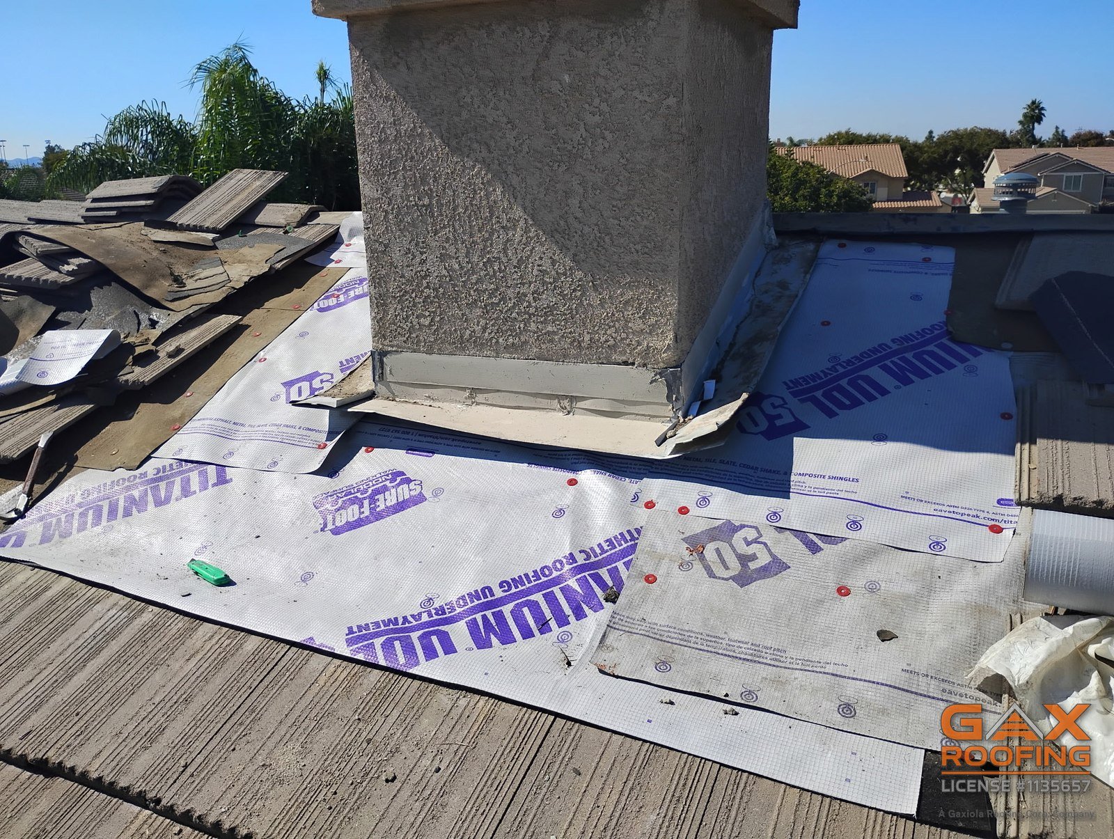 Tile lifted around a chimney on an Arcadia roof, exposing the underlayment and the base of the chimney before new flashing