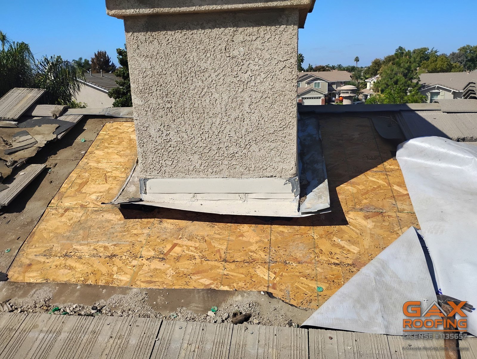 Deck and underlayment exposed at the base of a chimney on an Arcadia tile roof with the tile stacked aside during a GAX Roofing flashing repair