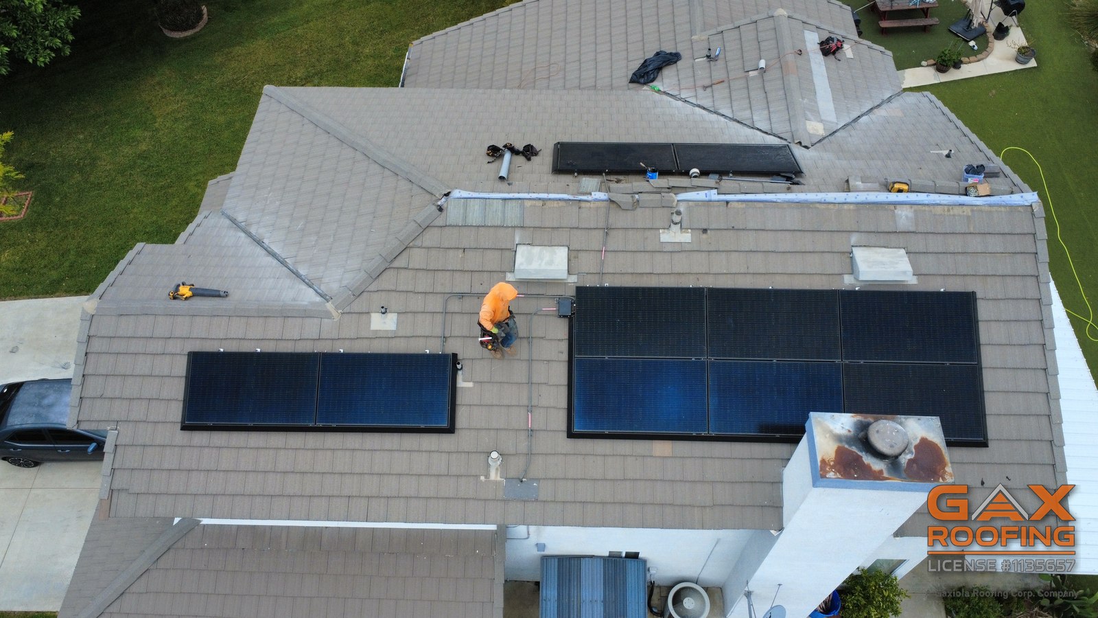 GAX Roofing crew working on a concrete tile roof with solar panels, aerial view