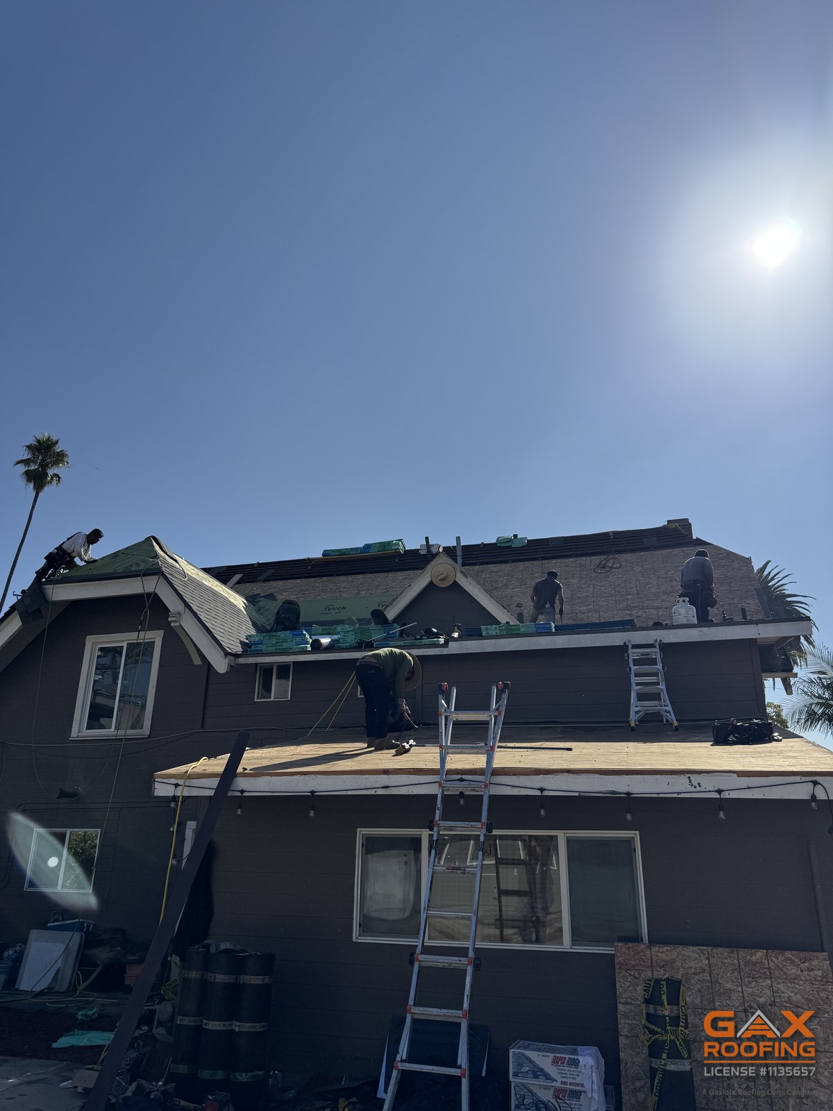 Cuadrilla de GAX Roofing trabajando un reemplazo de techo con escaleras colocadas en el alero