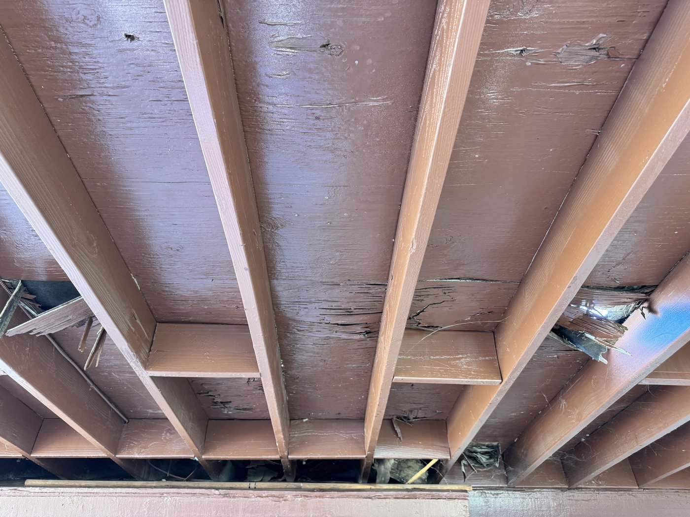 Water damaged and split rafters under a flat patio section with tile on it