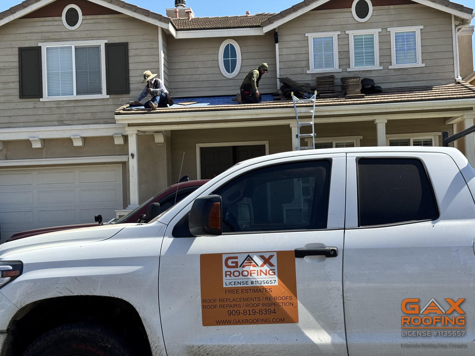 Vista desde la calle de una casa de dos pisos en Huntington Beach con la cuadrilla de GAX Roofing trabajando en el techo bajo del patio; el techo del segundo piso desagua sobre esta secci&oacute;n