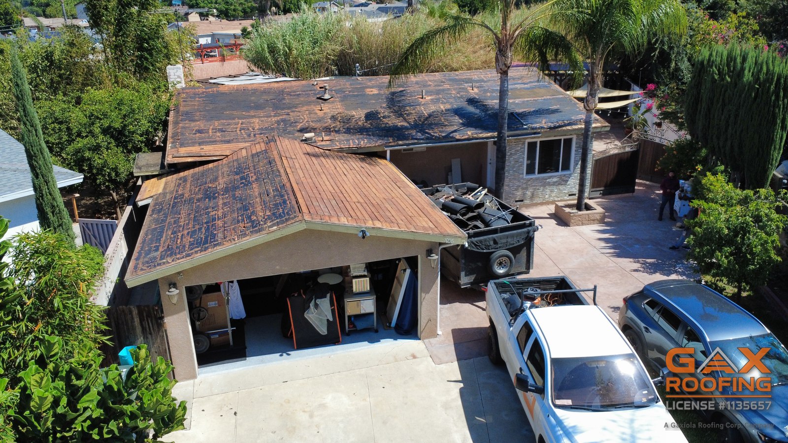 Aerial view of a Pomona house with the roof torn off and the debris trailer parked in the driveway