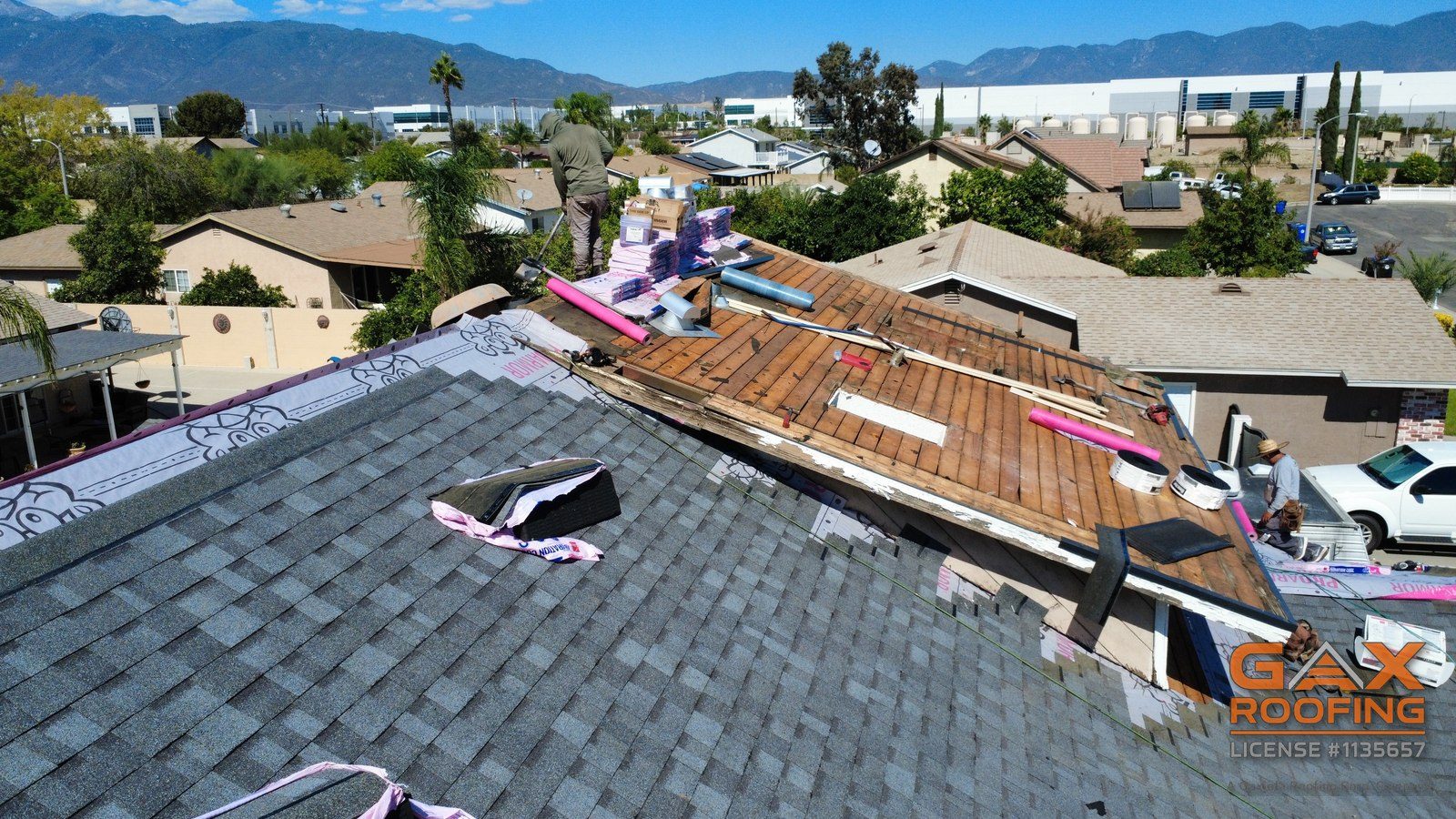 Cambio de techo de shingle en proceso en Fontana, California: shingles nuevos en el techo de abajo, el segundo piso descubierto hasta las tablas, monta&ntilde;as atr&aacute;s