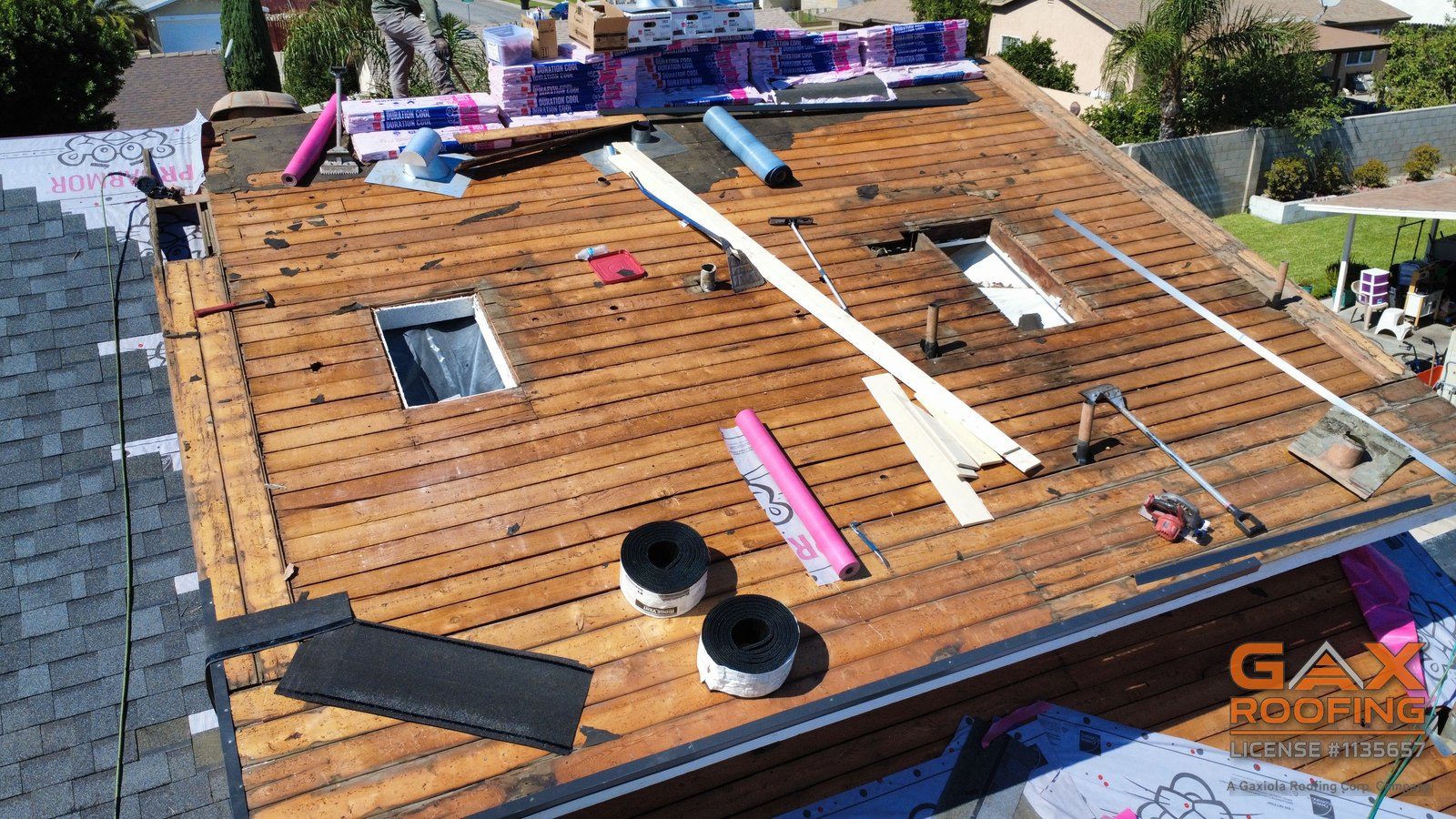 Entablado de tablas descubierto durante un cambio de techo de shingle en Fontana, con paquetes de Owens Corning Duration COOL listos y dos aberturas de tragaluz