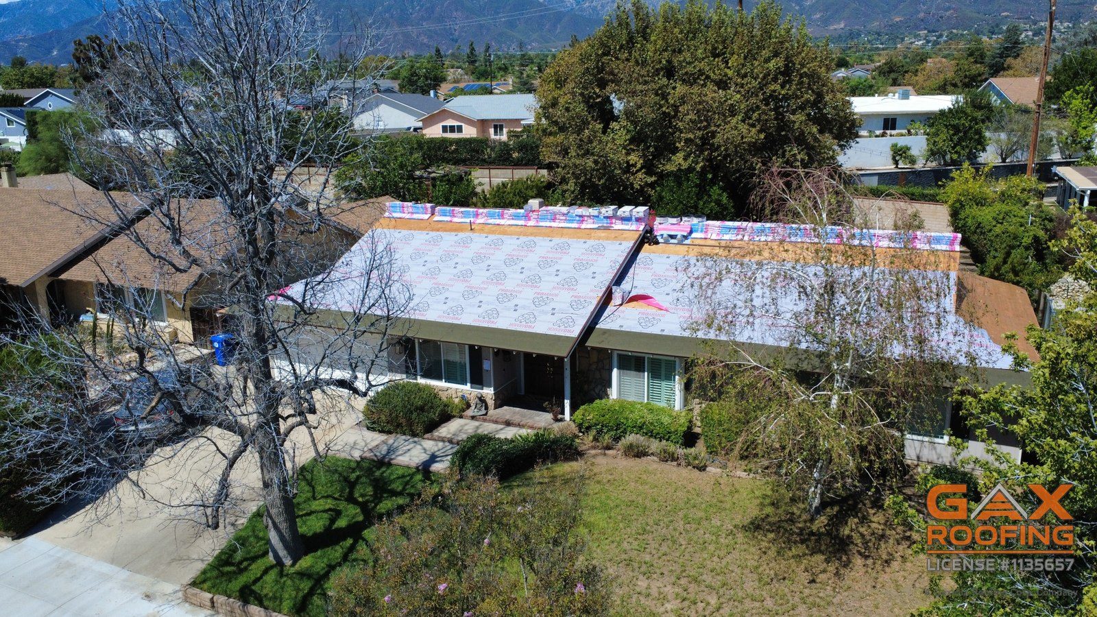 Rancho Cucamonga home during a shingle roof replacement, roof down to the deck with new underlayment going on, drone view from the front