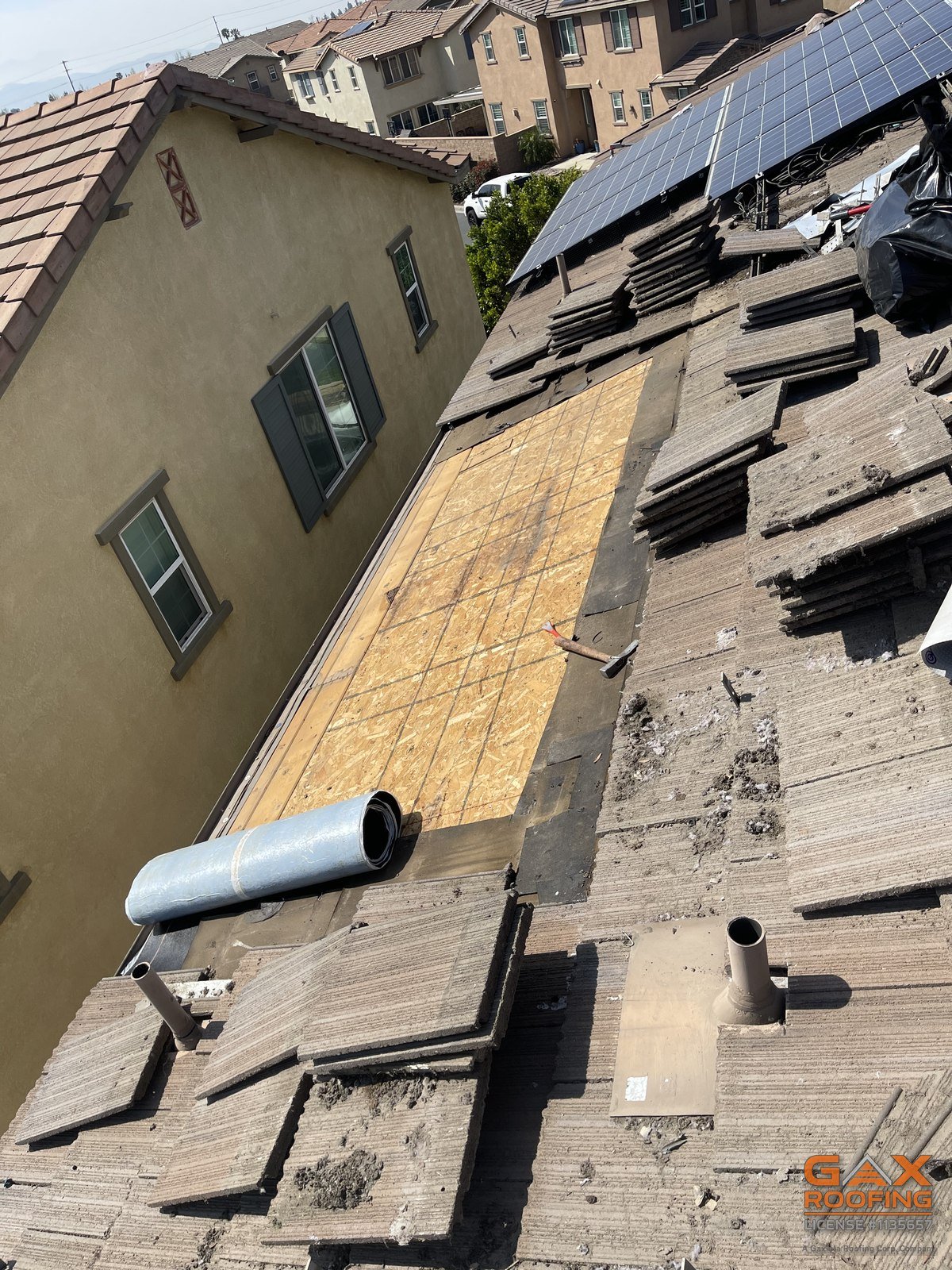 Tile stacked off and roof deck exposed beside a solar array during a San Dimas repair