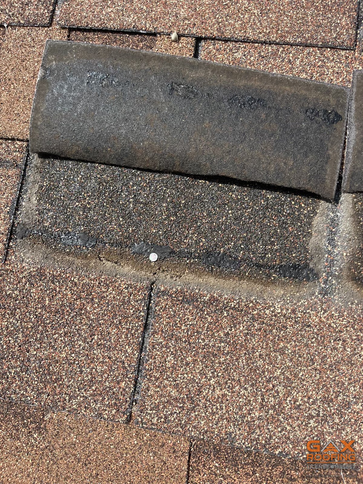 Close view of a flipped three tab shingle showing the sealant strip and an exposed nail head on the course above